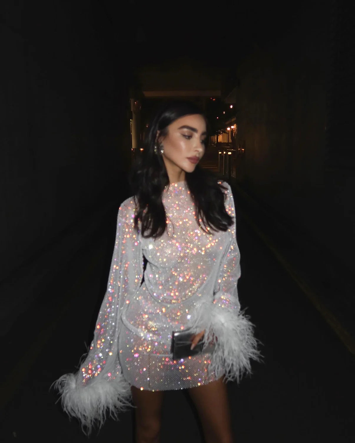 Indulge in the luxurious feel of the Feathers Mini Dress. This mini dress features wide sleeves and an ostrich feather that adds a touch of elegance. Crafted from open knit fabric with rhinestone embellishments throughout, this dress is perfect for making a statement at any event.