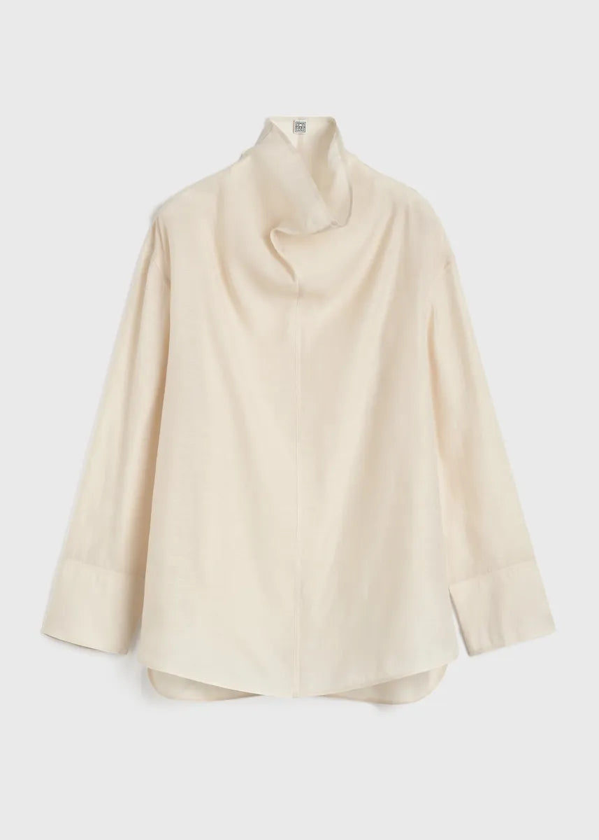 Elevate your wardrobe with this draped woven blouse by Toteme featuring a sophisticated funnel neck and relaxed dropped shoulders for effortless style. The curved hem with a longer back adds a contemporary silhouette, while the detachable cami lining offers versatility and comfort. Perfect for both casual and polished looks, this blouse combines elegance with adaptable wearability.