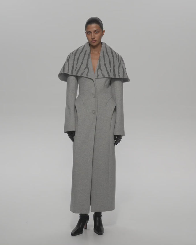 Discover timeless elegance with the Lorelle Coat in Gray, a sophisticated outerwear piece designed for the modern woman. This meticulously crafted coat features a fitted silhouette that flatters the figure, enhanced by detailed figured reliefs and striking accent barrels that add visual interest and dimension. The standout semi-circular cape collar creates a dramatic high neckline, perfect for layering and making a refined statement. 