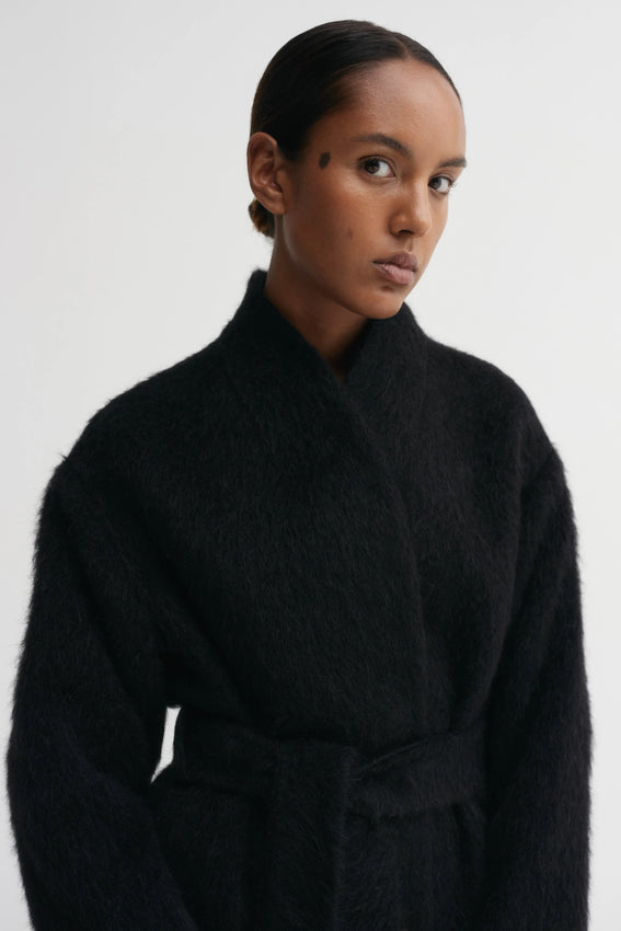 The Noorie Coat combines sumptuous comfort with timeless elegance. Crafted from a premium blend of thick alpaca and virgin wool, this piece features a naturally textured surface that resists dirt while maintaining its sophisticated appearance. The relaxed, slightly oversized silhouette is defined by a rounded neckline, gracefully dropped shoulders, and a wide belt that cinches the gently curved shape. Practical side-seam pockets and full interior lining complete the design. 
