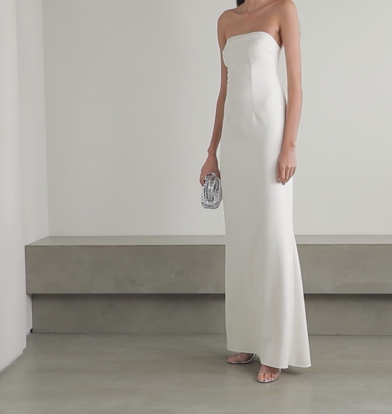 Effortless elegance meets modern romance in this stunning strapless crepe gown by Safiyaa. Designed with flattering curved seams that sculpt and define, this dress glides gracefully to the floor—perfect for a confident walk down the aisle. The smooth, luxurious crepe fabric drapes beautifully while the strapless neckline keeps the focus on you. Pair it with a delicate veil for the ceremony, then slip on the matching jacket for a chic reception transformation. 