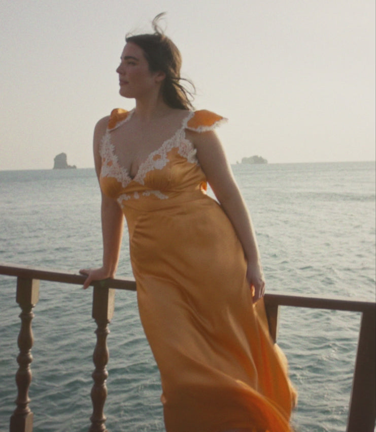 This luxurious silk satin dress features an elegant plunging neckline and cap sleeves adorned with intricate floral lace detailing. The tailored bodice is secured with a concealed side zipper and adjustable back tie, flowing into a gracefully bias-cut skirt. In a stunning tangerine shade, the Fiona Dress effortlessly transitions from formal events to refined casual occasions, adding radiance and elegance to your collection.