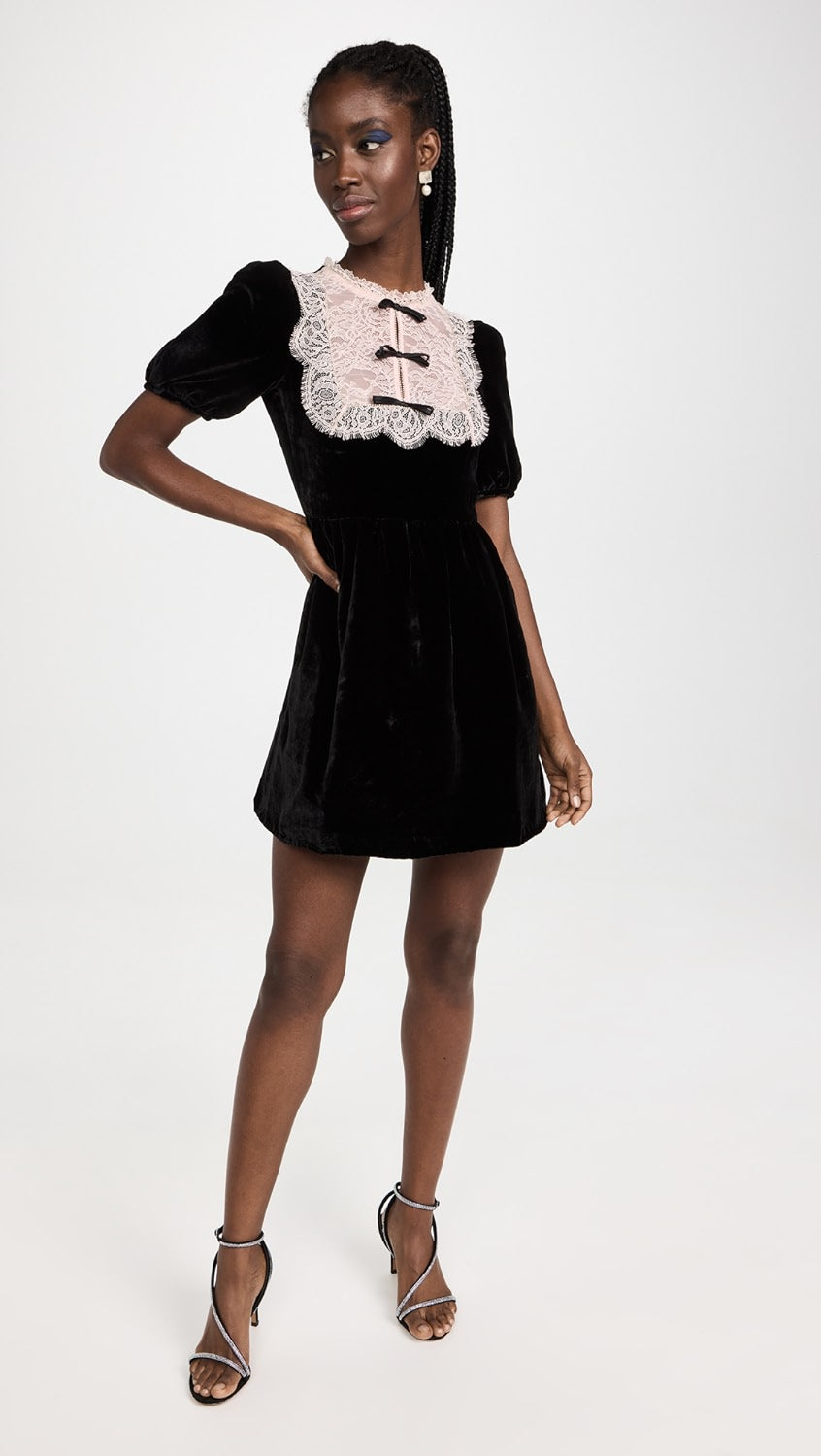 The Cherie Mini Dress is crafted from lightweight non-stretch velvet, giving it an elegant and luxurious feel. The lace yoke with crystal trim and fixed bow accents adds a touch of glamour. The short puff sleeves with button cuffs and round ruffle neckline give the dress a feminine and playful look. 